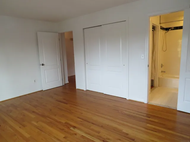 a view of an empty room with wooden floor and a bathroom