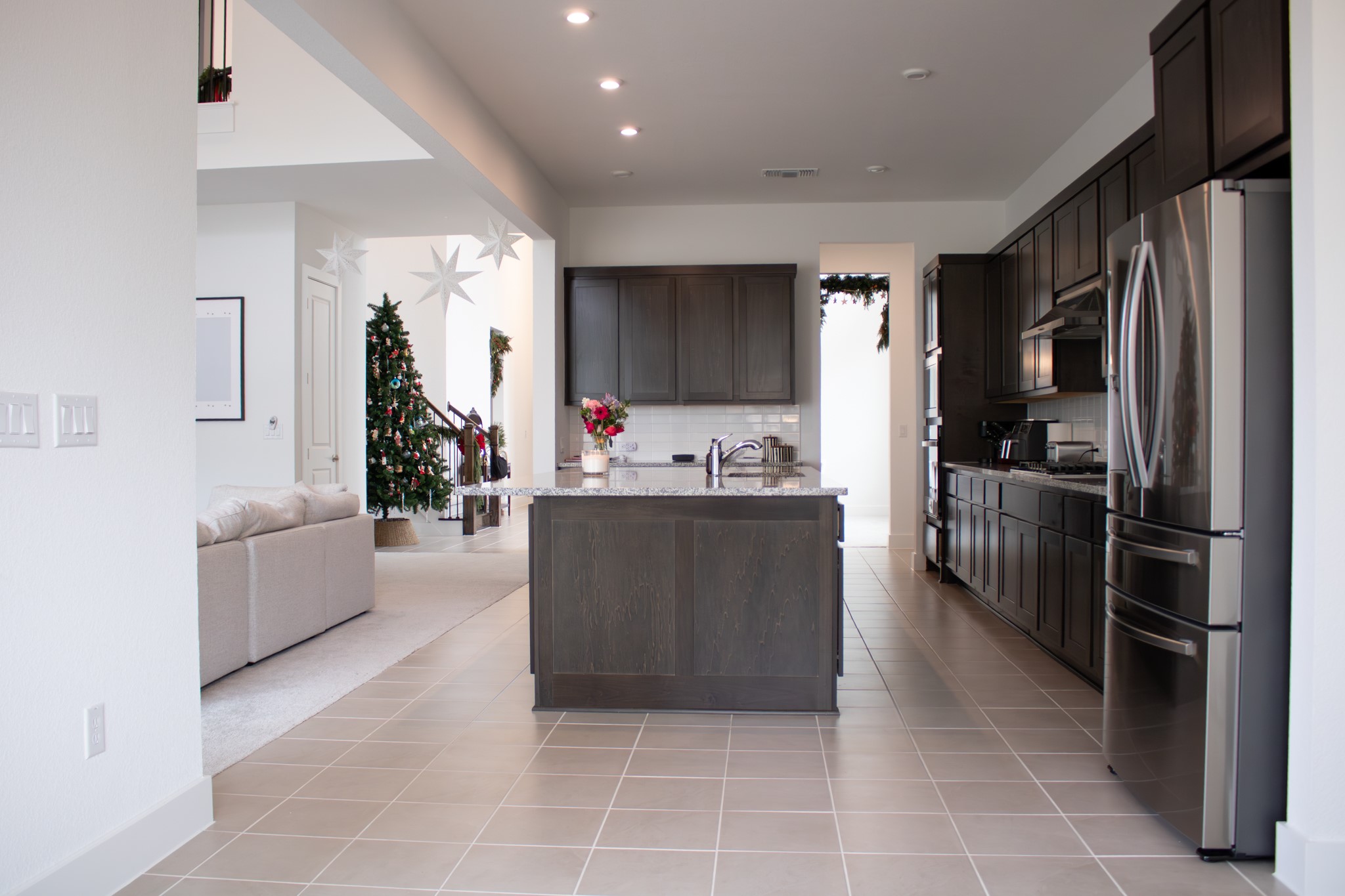 1709 Novara Trail Leander, TX 78641 - Photo 19 of 40 Kitchen featuring freestanding refrigerator, light tile patterned floors, dark wood finish cabinets, tasteful backsplash, and a center island with sink