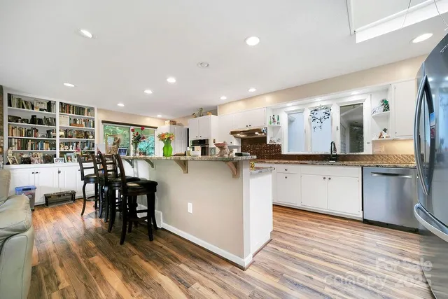 a kitchen with stainless steel appliances kitchen island granite countertop a stove a sink a refrigerator and white cabinets with wooden floor