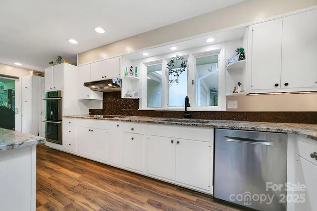 a large white kitchen with stainless steel appliances granite countertop a stove and a sink