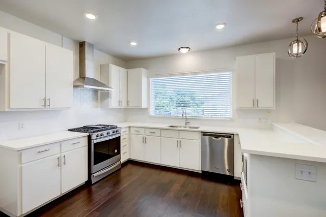 a kitchen with stainless steel appliances granite countertop a sink a stove a refrigerator and white cabinets with wooden floor