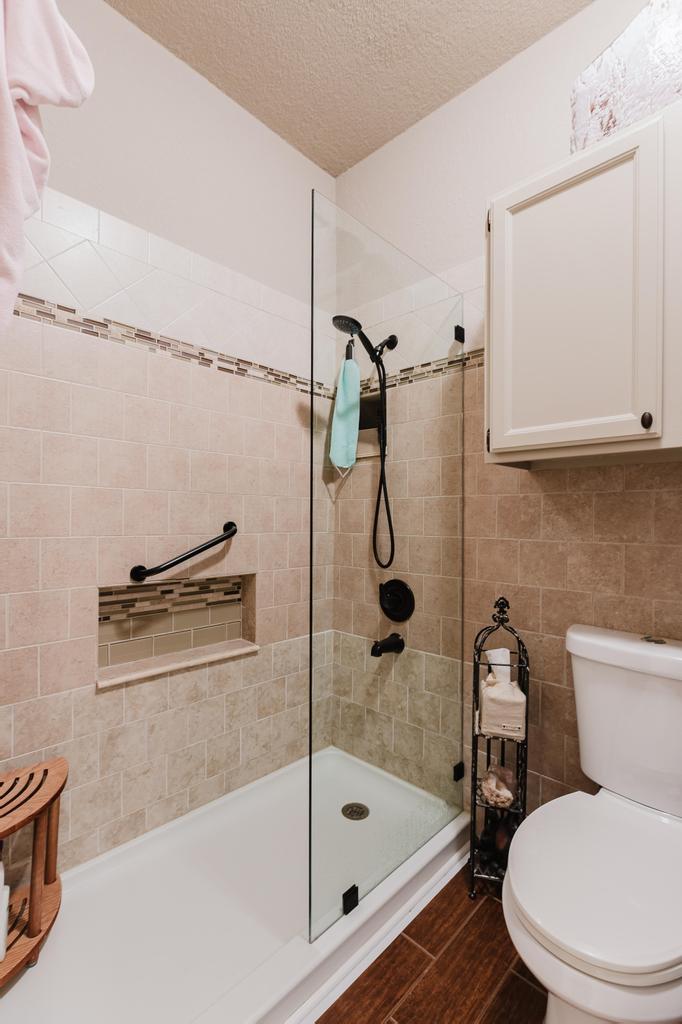 10819 Crown Colony Drive, Unit 40 Austin, TX 78747 - Photo 21 of 38 Bathroom with a textured ceiling, a tile shower, wood finish floors, and tile walls