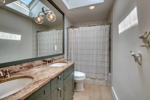 a bathroom with a granite countertop toilet a sink a mirror and shower curtain
