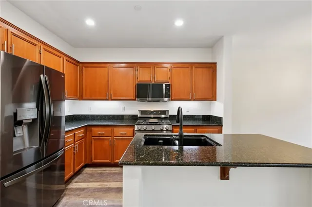 a kitchen with stainless steel appliances granite countertop a refrigerator a stove and a sink with wooden cabinets