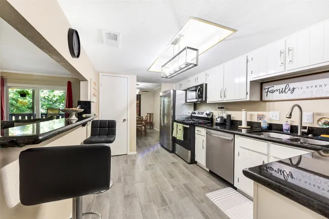 a kitchen with granite countertop a stove a sink a refrigerator cabinets and living room view