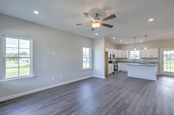 an empty room with wooden floor and kitchen view