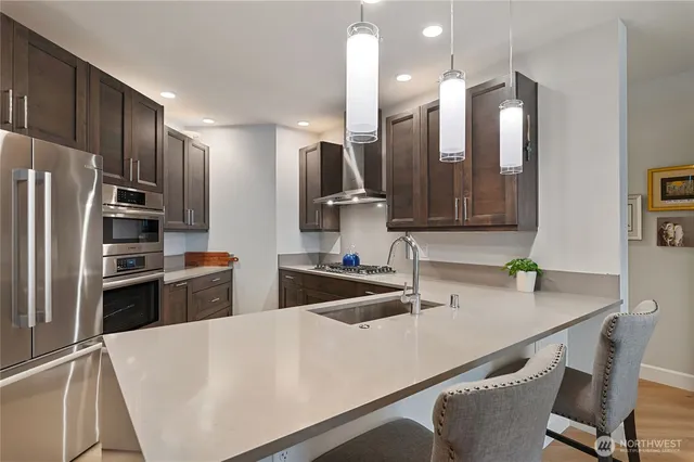 a kitchen with stainless steel appliances a sink a stove a refrigerator cabinets and chairs