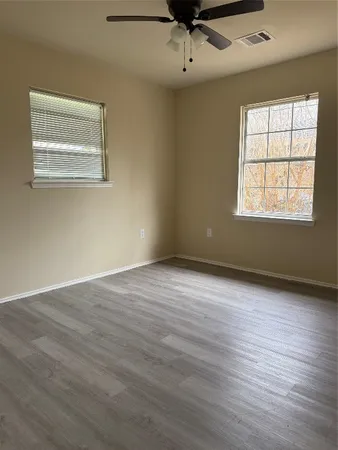 an empty room with wooden floor chandelier fan and windows