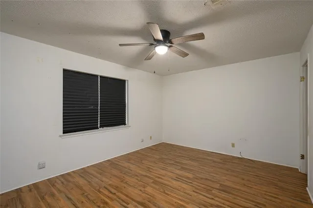 a view of an empty room with wooden floor and a ceiling fan
