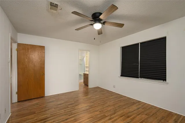 a view of an empty room with wooden floor and a ceiling fan