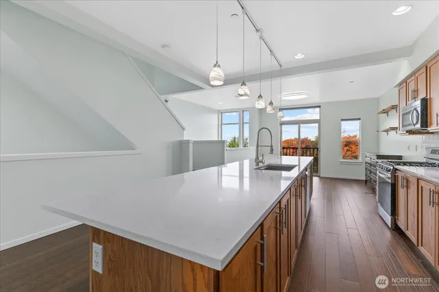 a kitchen with stainless steel appliances granite countertop a refrigerator a sink dishwasher a stove and a dining table with wooden floor