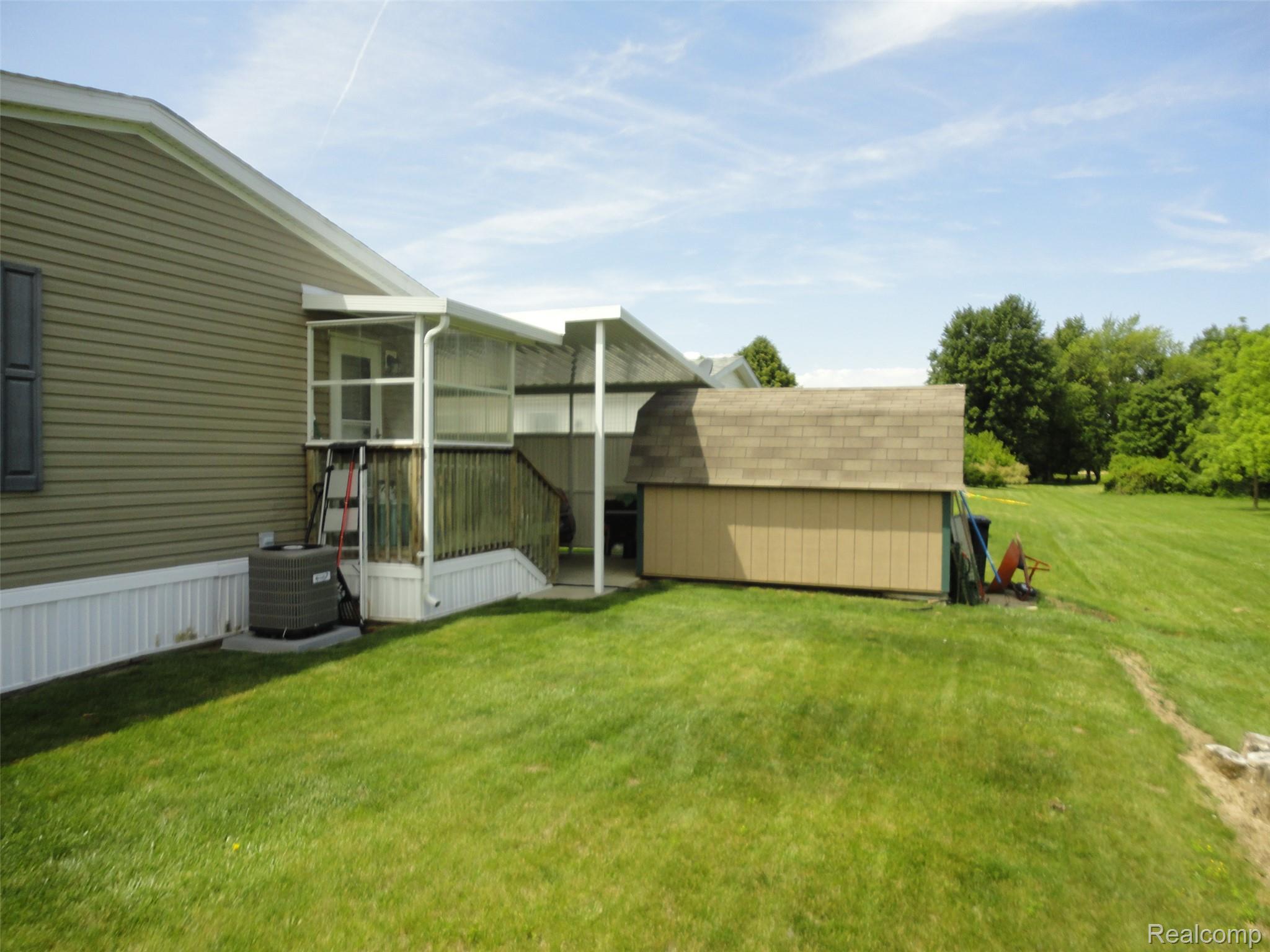 463 Edinborough Temperance, MI 48182 - Photo 20 of 23 Exterior featuring tan siding, a screened porch with white railing, and an adjacent storage shed with a shingled roof