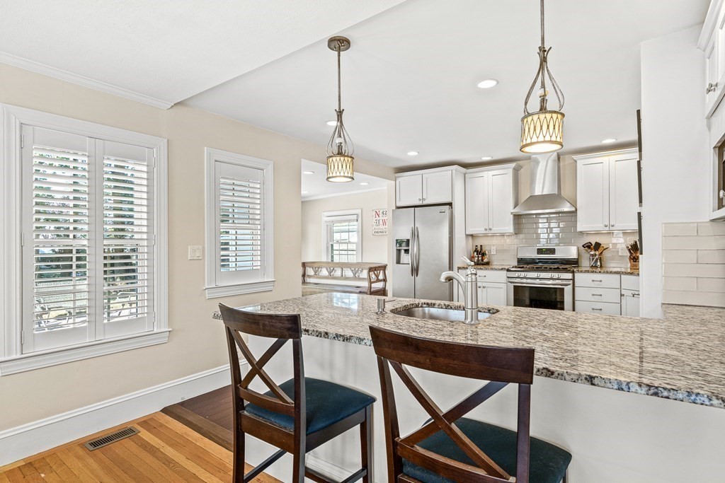 7 Perkins Avenue Reading, MA 01867 - Photo 11 of 42 a kitchen with stainless steel appliances granite countertop a stove a sink a microwave a dining table and chairs with wooden floor