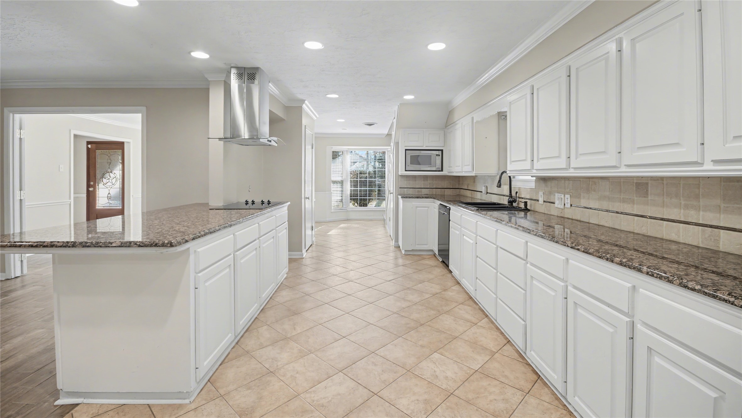 1431 Walnut Lane Houston, TX 77339 - Photo 12 of 47 Bright and spacious kitchen with white cabinetry, granite countertops, and tile flooring. It features modern stainless steel appliances, including a built-in microwave and stove. The room is well-lit with recessed lighting and has a large window allowing natural light to fill the space.