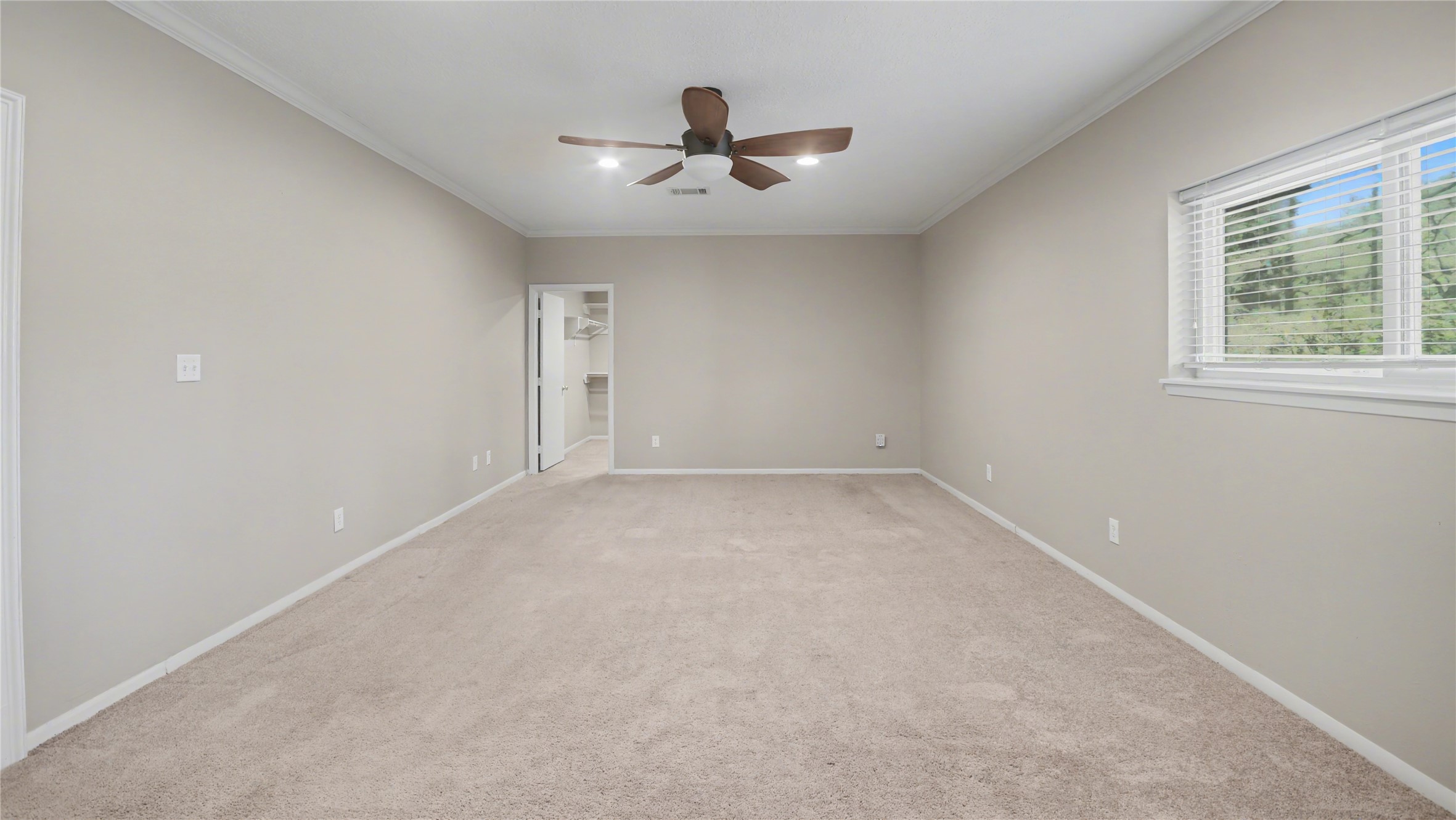 1431 Walnut Lane Houston, TX 77339 - Photo 20 of 44 This spacious bedroom offers a serene retreat with soft carpeting, a modern ceiling fan, and abundant natural light streaming through a large window, seamlessly leading to a walk-in closet.