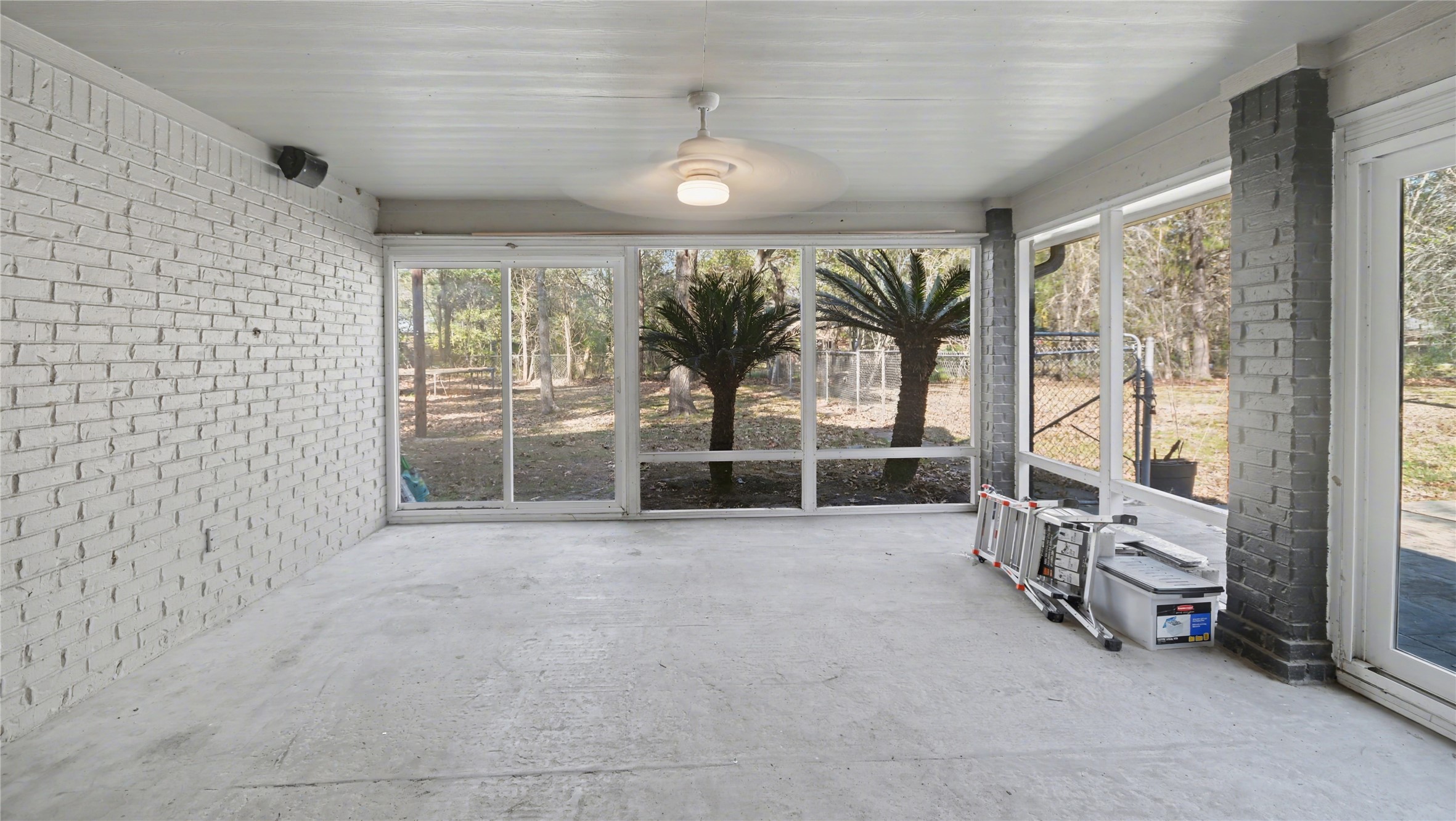 1431 Walnut Lane Houston, TX 77339 - Photo 41 of 46 Sunroom with large windows, white brick walls, and a ceiling fan. It offers a view of a landscaped backyard, making it an ideal space for relaxation or entertaining.