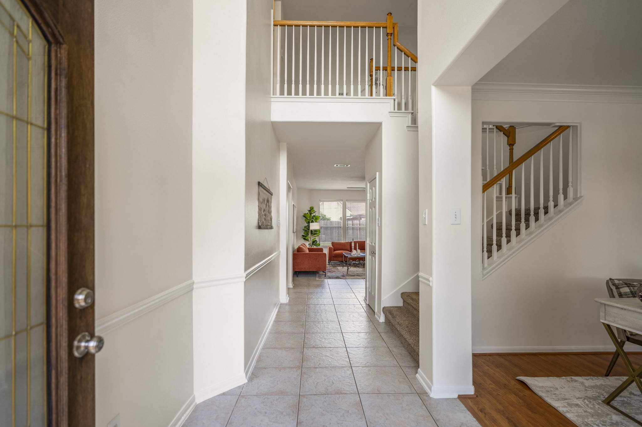 19106 South Rim Trail Spring, TX 77388 - Photo 4 of 50 Stepping inside, the double-height foyer immediately introduces the home’s open feel, with the staircase rising to the right and the upstairs railing overlooking the entry below. Just off the foyer, the front room adds flexible space near the main entrance, while the tiled hallway carries your eye straight back toward the living room, where the main gathering spaces and natural light begin to come into view.