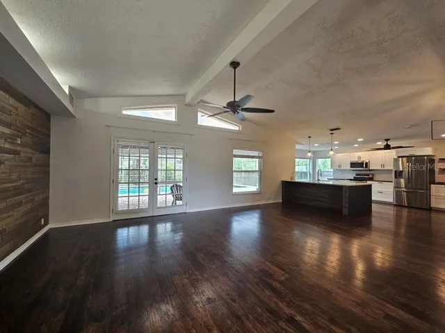 an empty room with wooden floor and kitchen view