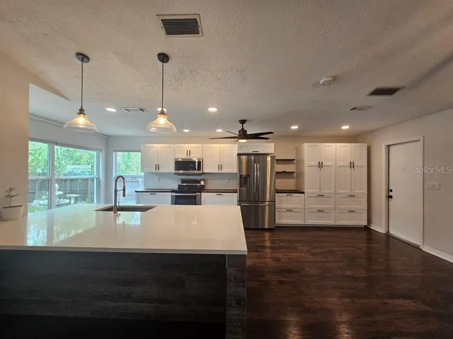a open kitchen with kitchen island a stove a refrigerator a sink dishwasher with a dining table and chairs with wooden floor