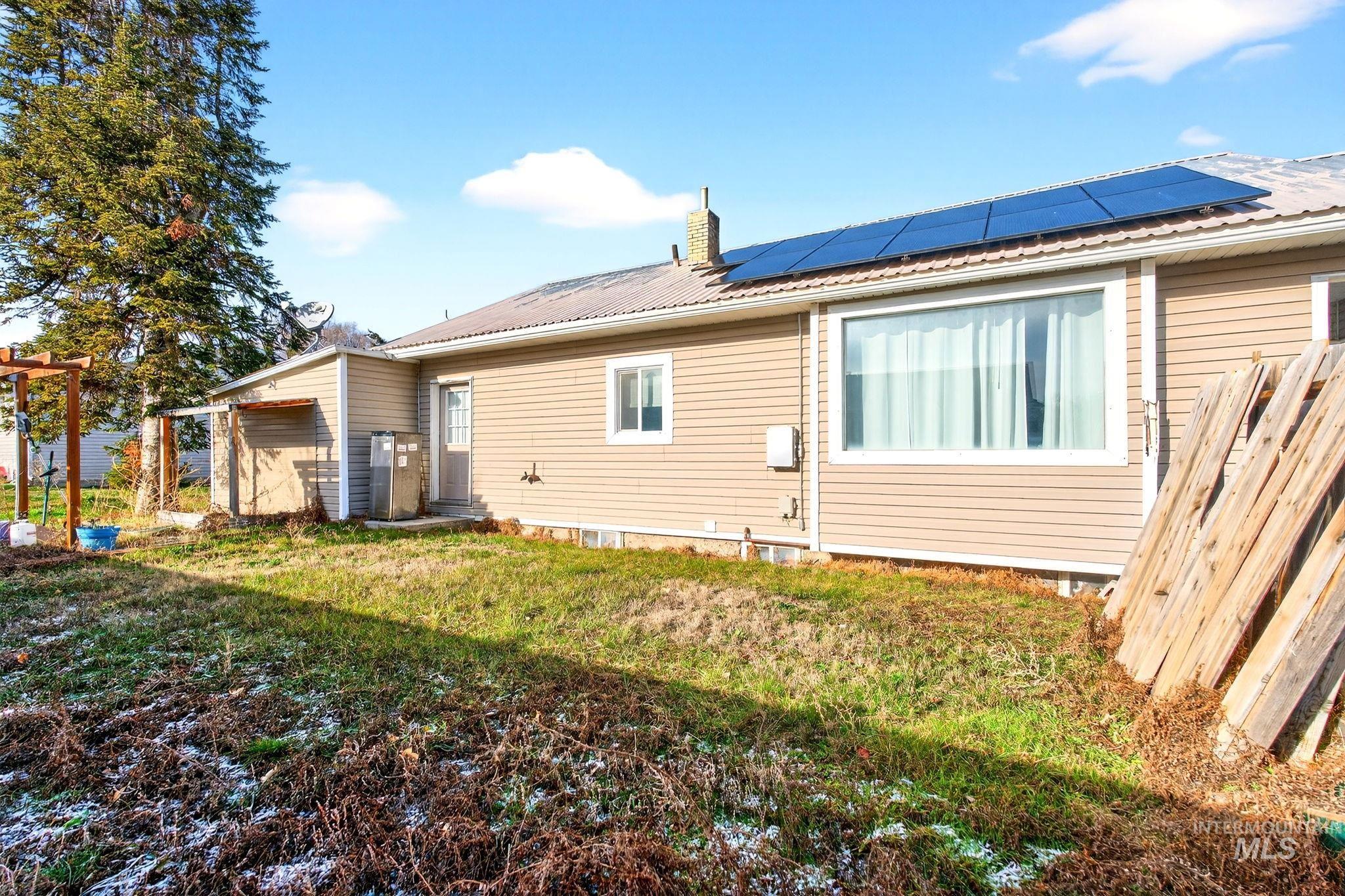 208 South 4th W Street Preston, ID 83263 - Photo 33 of 38 Back of house with roof mounted solar panels, a metal roof, a chimney, and a lawn