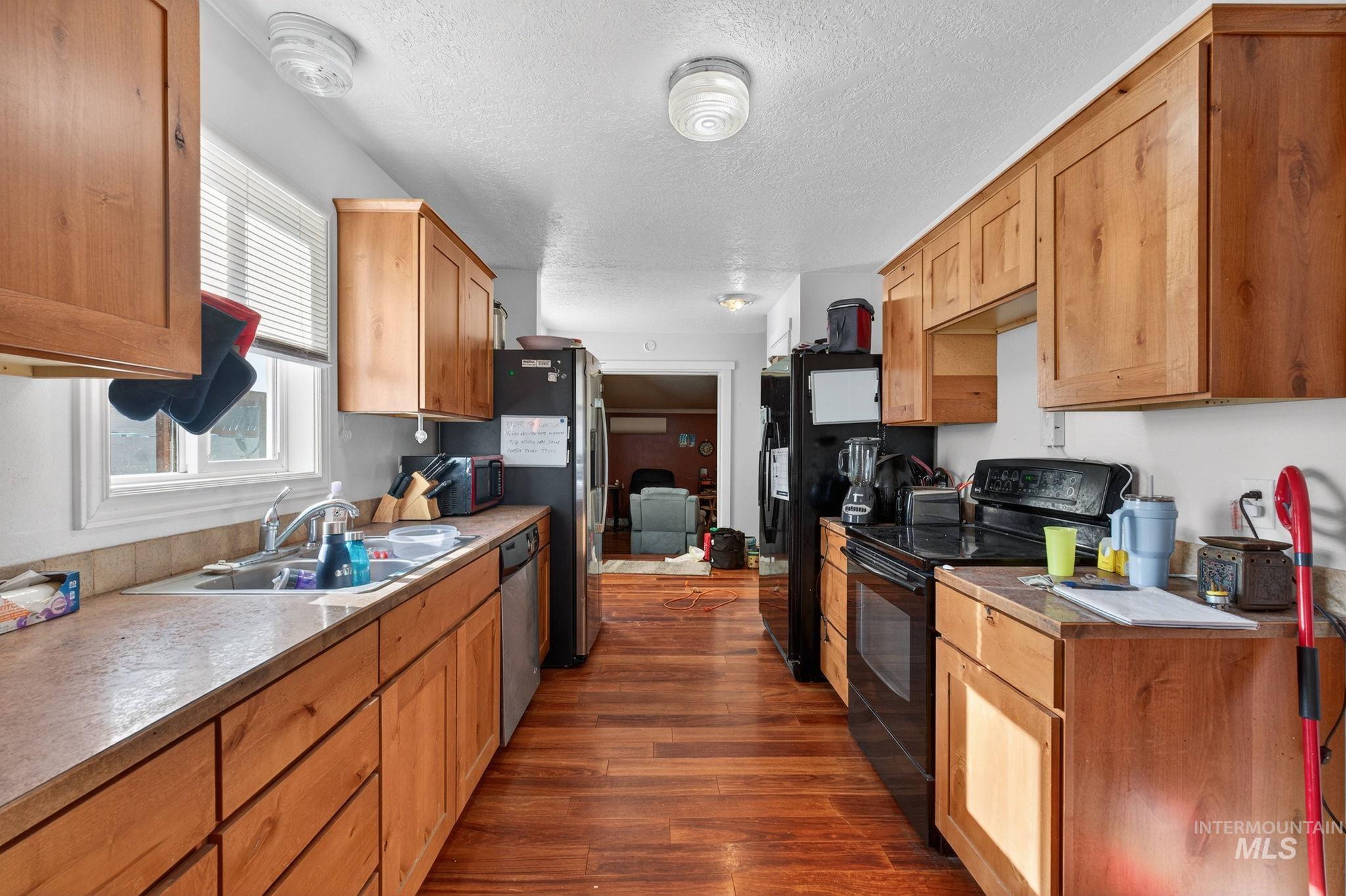 208 South 4th W Street Preston, ID 83263 - Photo 8 of 38 Kitchen with black appliances, a textured ceiling, dark wood-style flooring, brown cabinets, and light countertops