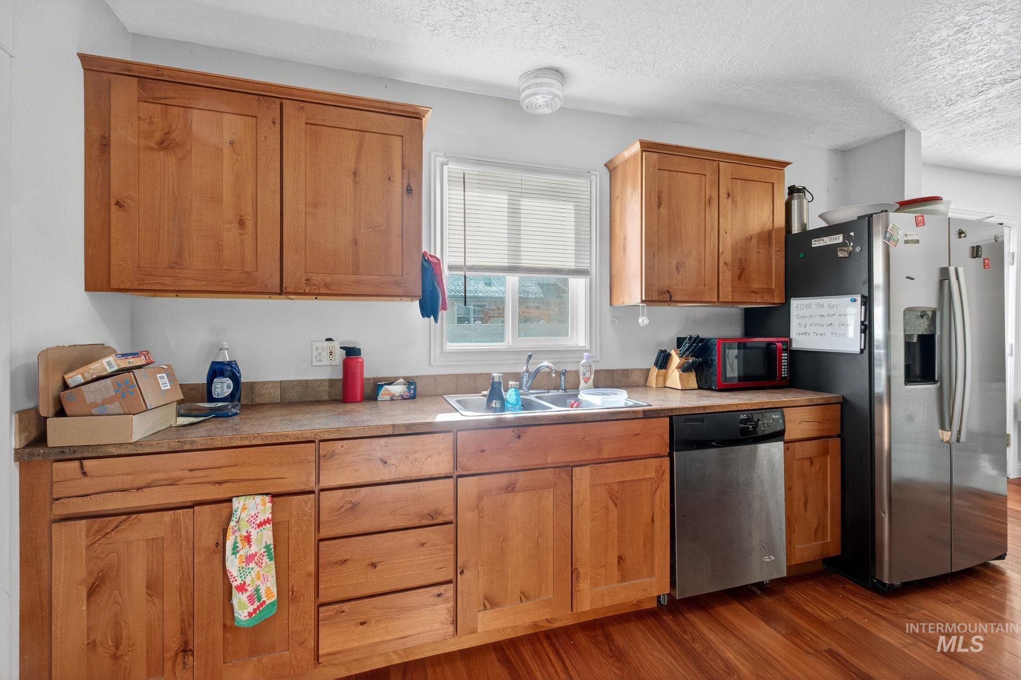 208 South 4th W Street Preston, ID 83263 - Photo 9 of 38 Kitchen featuring stainless steel appliances, dark wood-style flooring, a textured ceiling, light countertops, and brown cabinets