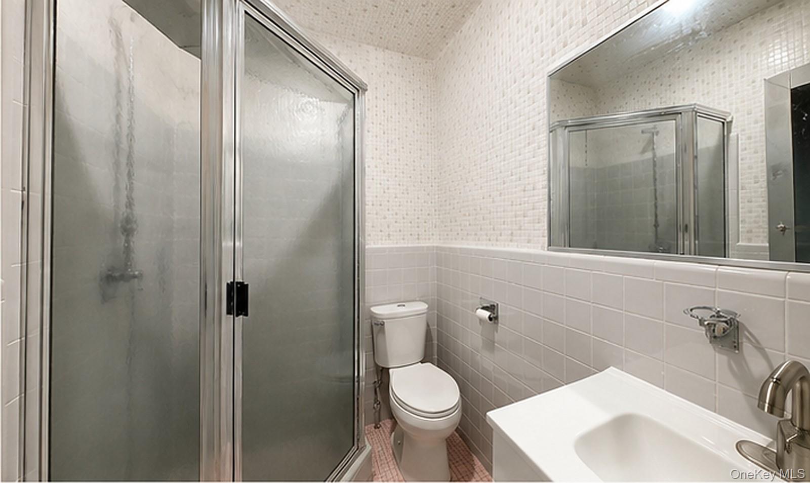 217-41 Stewart Road Queens, NY 11364 - Photo 2 of 11 Chrome-framed glass shower enclosure, white ceramic tile walls, integrated vanity sink, and a wall-mounted mirror