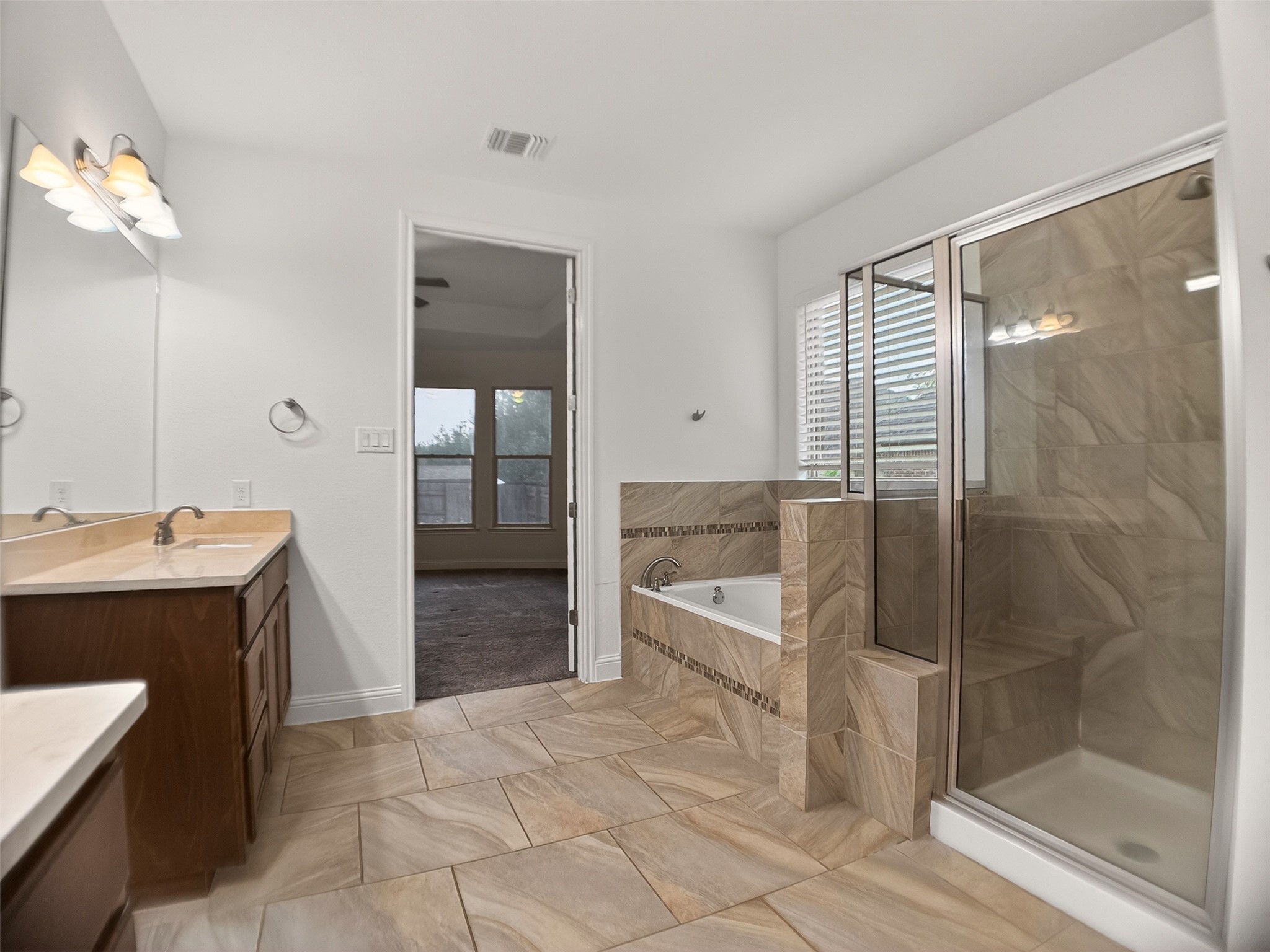 1505 Long Shadow Lane Georgetown, TX 78628 - Photo 14 of 28 Bathroom featuring light-toned tile flooring, a built-in soaking tub with tile surround, a glass-enclosed shower with tile walls and built-in bench, and a vanity with a light-colored countertop and dark wood-finish cabinetry