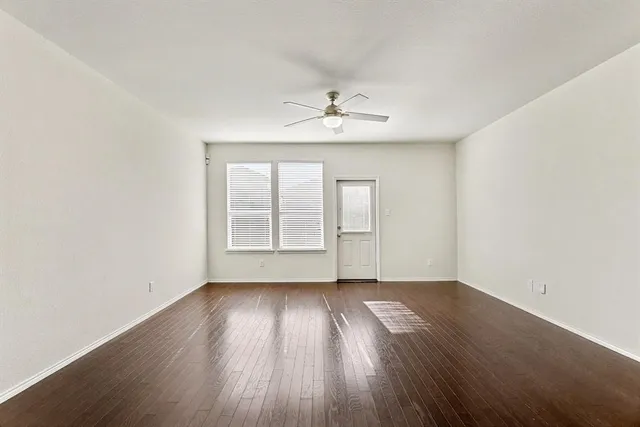 an empty room with wooden floor chandelier fan and windows