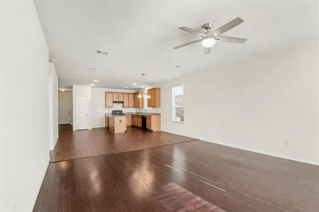 a view of an empty room with wooden floor and a ceiling fan