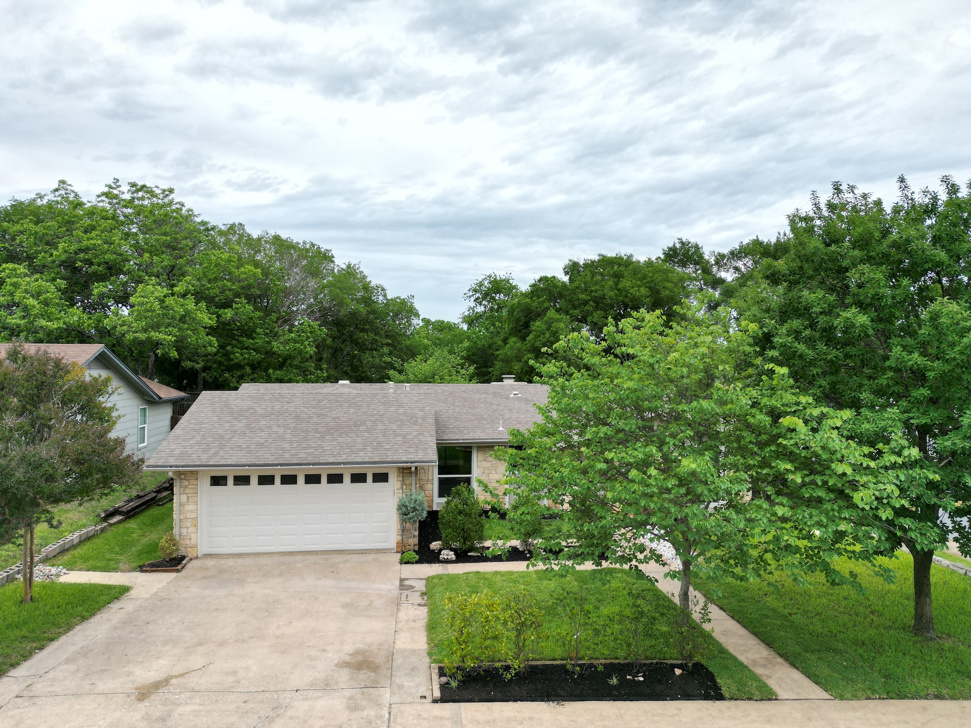1608 Springer Lane Austin, TX 78758 - Photo 2 of 35 Stone facade home featuring an attached garage with a white door, a paved driveway, and mature landscaping