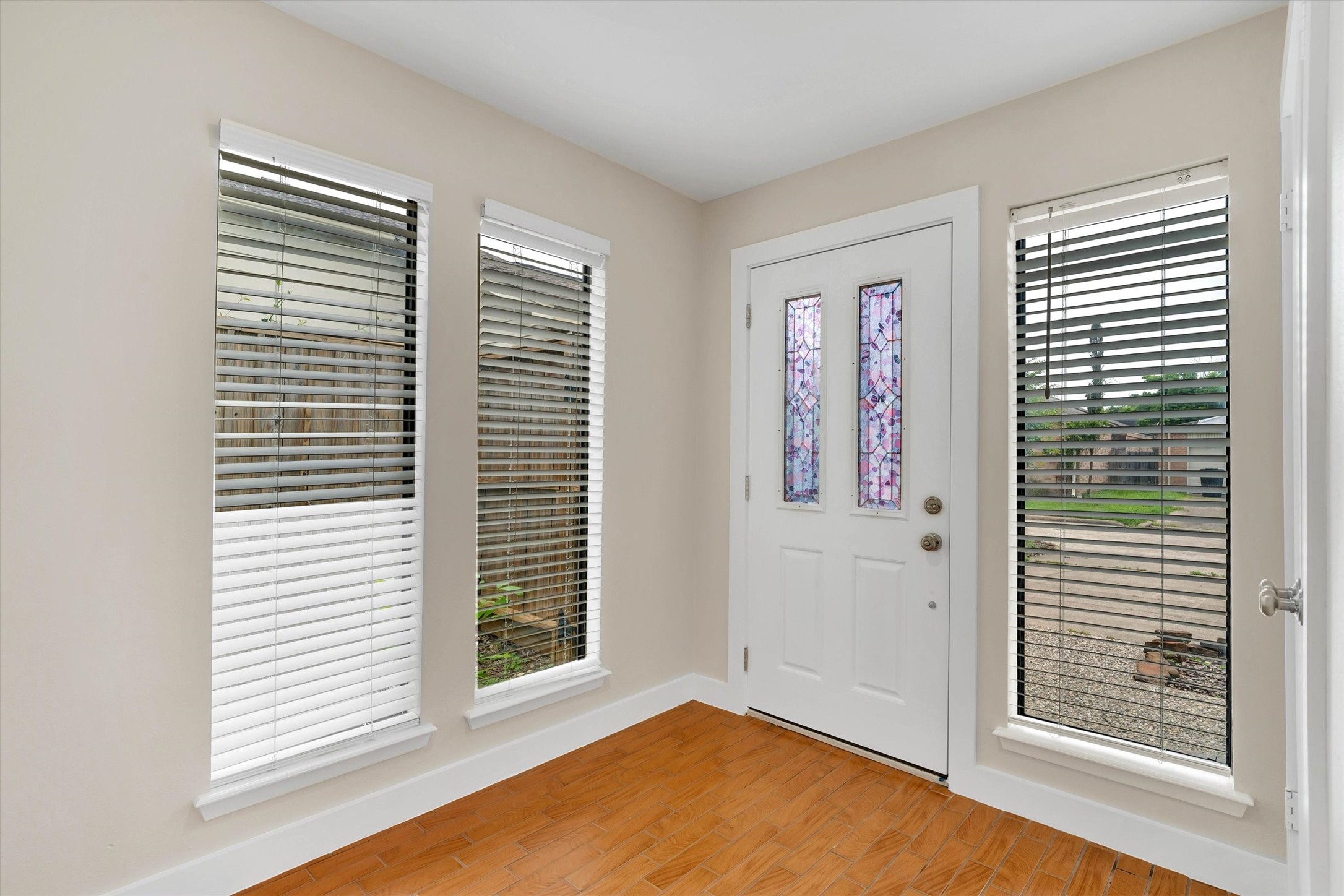 2163 Paso Rello Drive Houston, TX 77077 - Photo 9 of 45 Bright entryway with a white door featuring decorative glass panels. Flanked by three vertical windows with blinds, allowing natural light to fill the space. The flooring is a warm-toned wood, creating an inviting atmosphere.