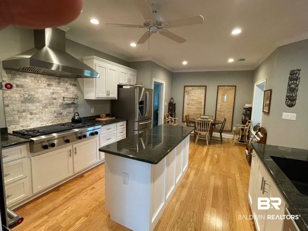 6426 East Quarry Drive Elberta, AL 36530 - Photo 5 of 19 Kitchen featuring white cabinetry, light wood-type flooring, dark stone counters, a center island, and wall chimney exhaust hood