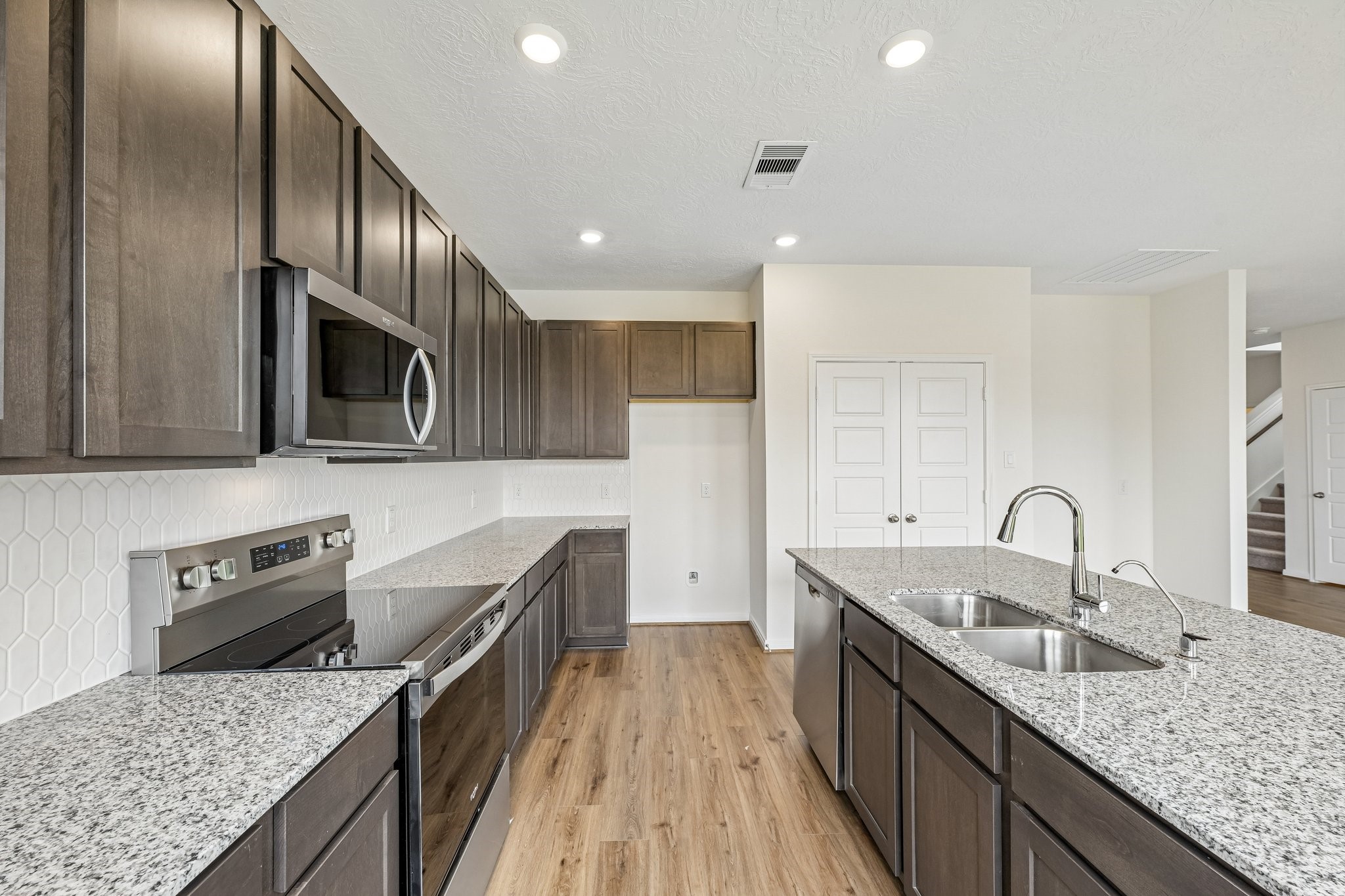 2503 Spruce Hl Road Beasley, TX 77417 - Photo 12 of 25 This kitchen boasts high ceilings, Woodmont Dakota cabinets in Smoke stain, Luna Pearl Granite countertops, stainless steel Whirlpool appliances, a modern Daltile backsplash, recessed lighting, an added breakfast bar to kitchen countertop, and a pantry—all overlooking the expansive Great Room.