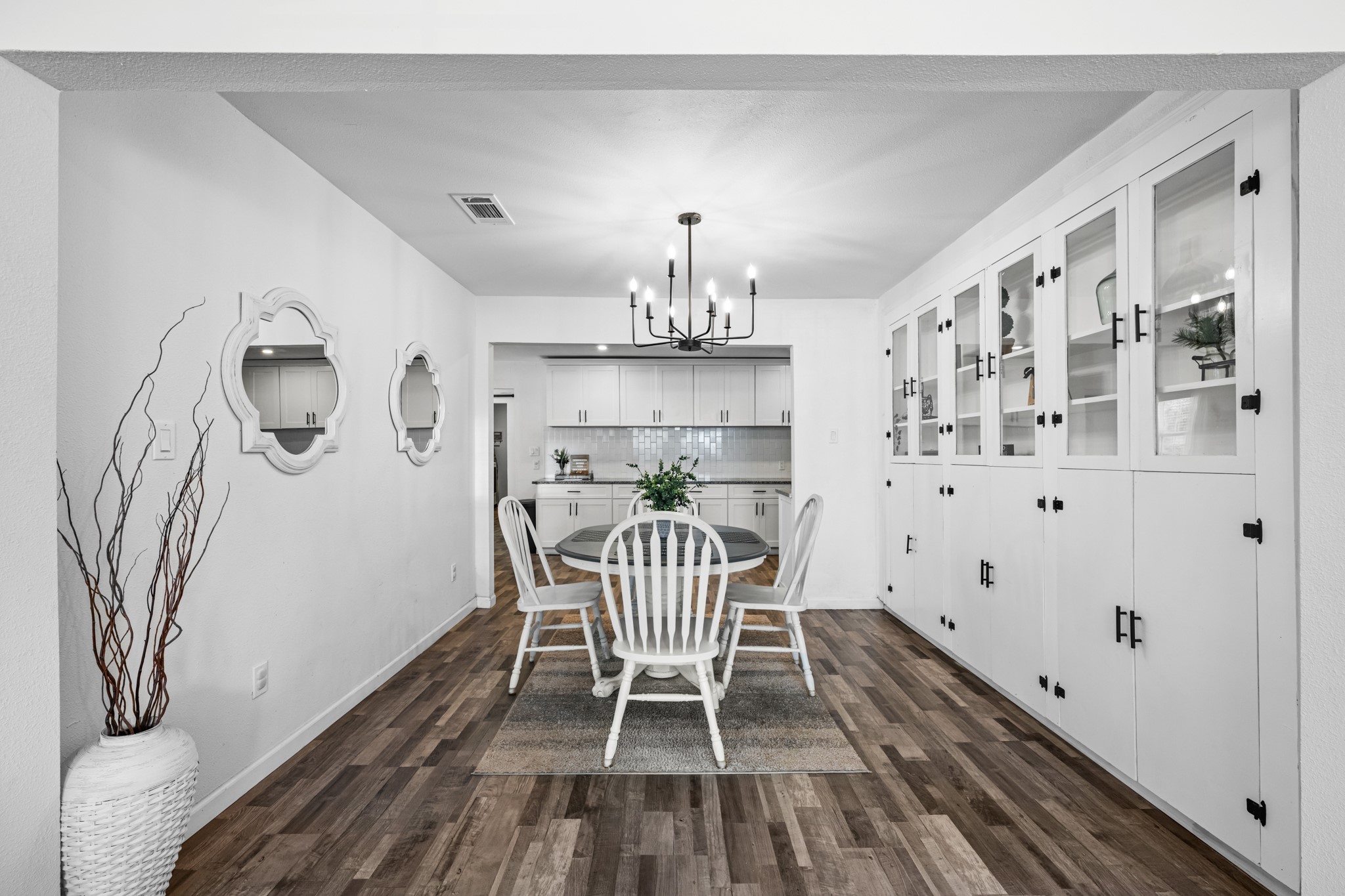 729 Kyle Angleton, TX 77515 - Photo 7 of 36 This dining area features a modern chandelier, built-in cabinets for ample storage, and a cozy table setup. The space is bright with white walls and wood-look vinyl plank flooring, seamlessly connecting to the kitchen.