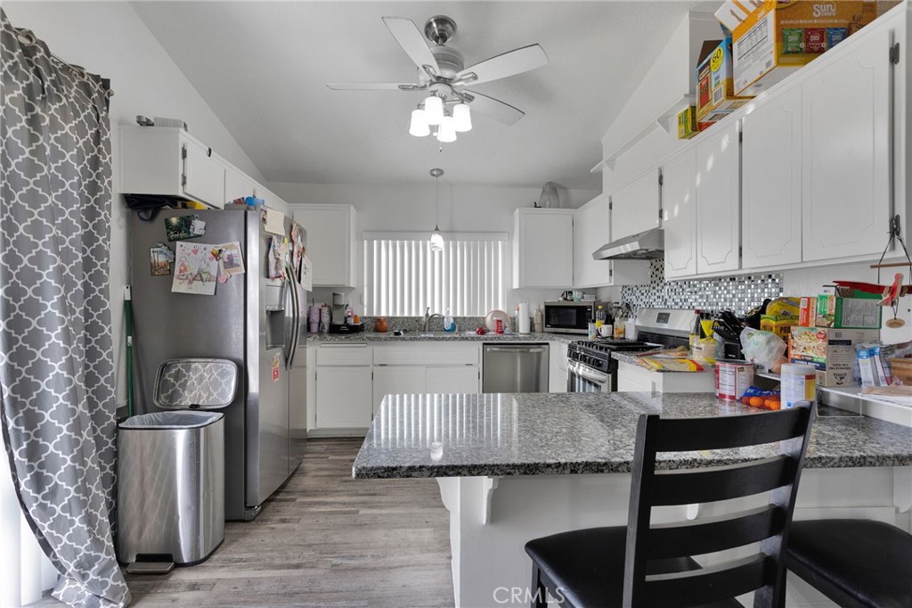 22517 Ojai Road Apple Valley, CA 92308 - Photo 14 of 25 a kitchen with stainless steel appliances granite countertop a refrigerator a stove a sink dishwasher and white cabinets with wooden floor