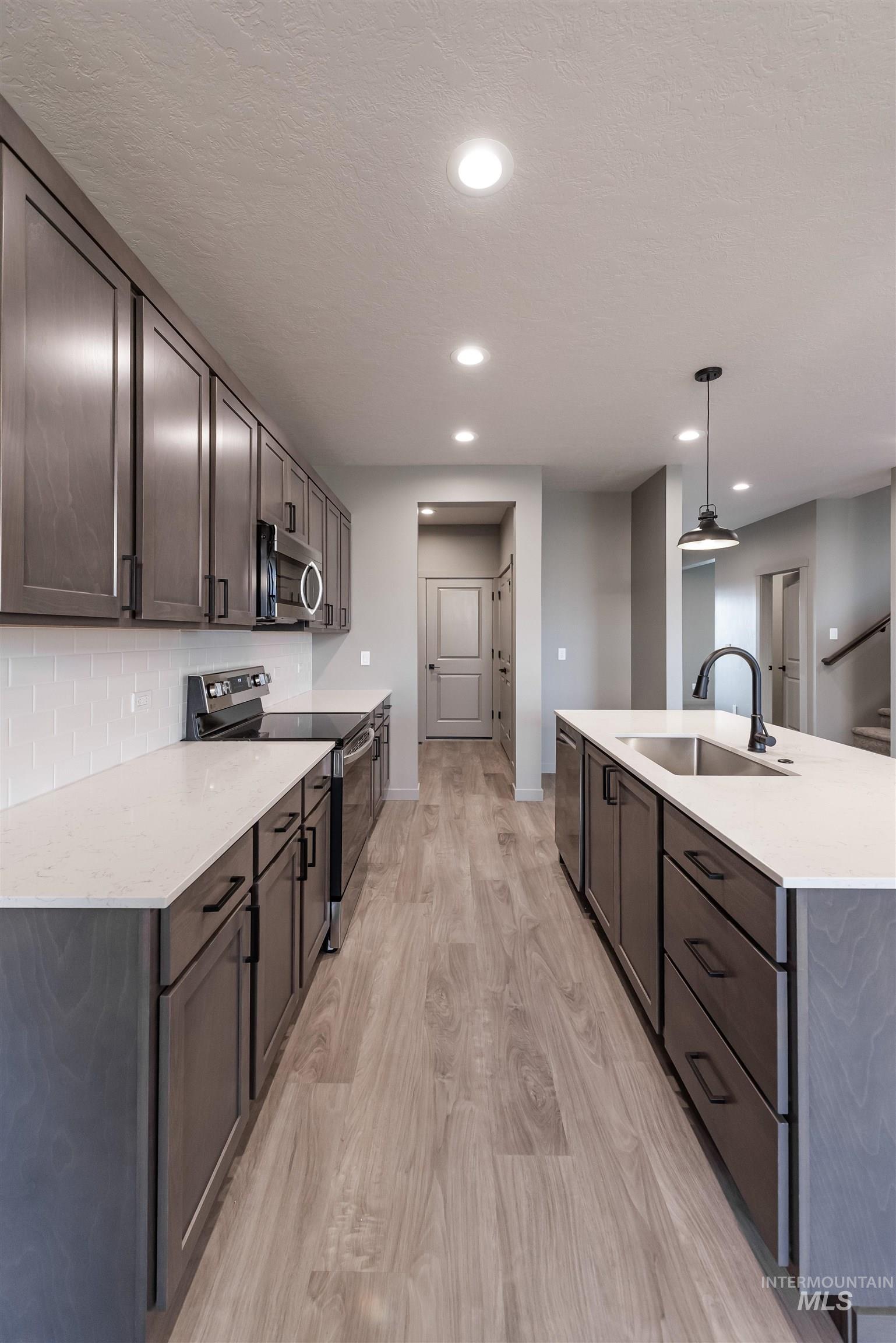 360 South Bumper Way Boise, ID 83716 - Photo 7 of 34 Kitchen with appliances with stainless steel finishes, pendant lighting, light stone counters, light wood-style flooring, and a kitchen island with sink