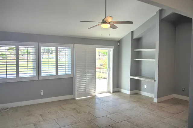 an empty room with chandelier fan and windows