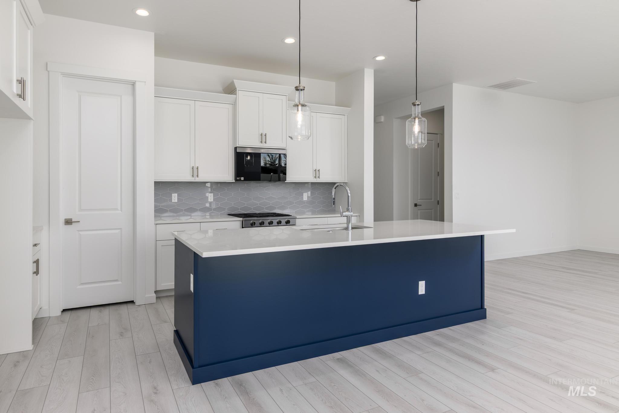 1195 West Switchgrass Drive Meridian, ID 83642 - Photo 5 of 11 Kitchen with white cabinets, hanging light fixtures, a kitchen island with sink, backsplash, and light stone counters