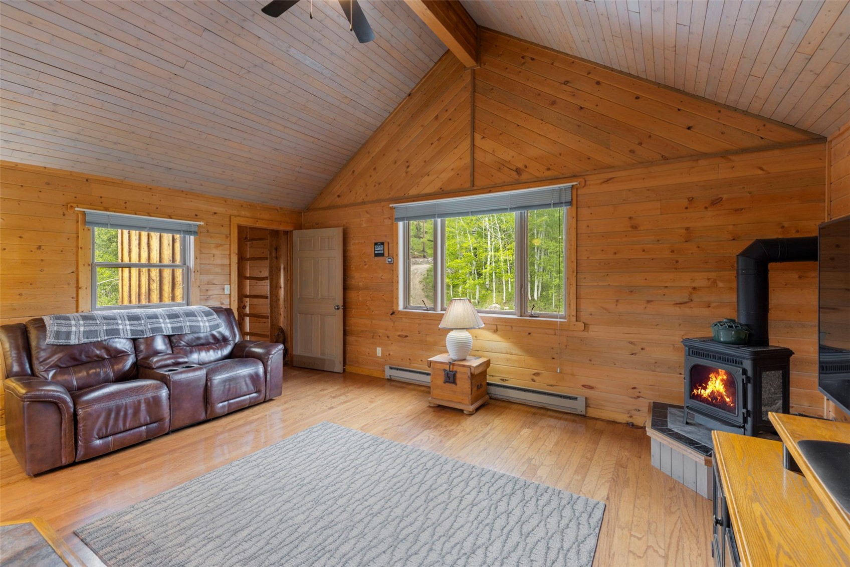 1516 Blue Ridge Road Silverthorne, CO 80498 - Photo 10 of 50 Living room with wooden walls, a wood stove, a ceiling fan, light wood-type flooring, and a baseboard heating unit