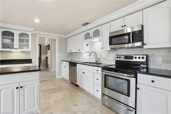 a kitchen with stainless steel appliances granite countertop grey cabinets a stove a sink and a microwave