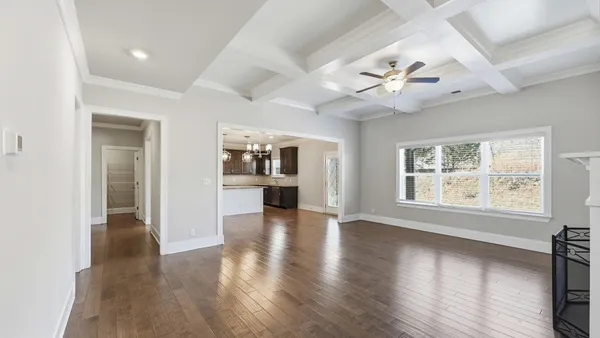 an empty room with wooden floor chandelier and windows