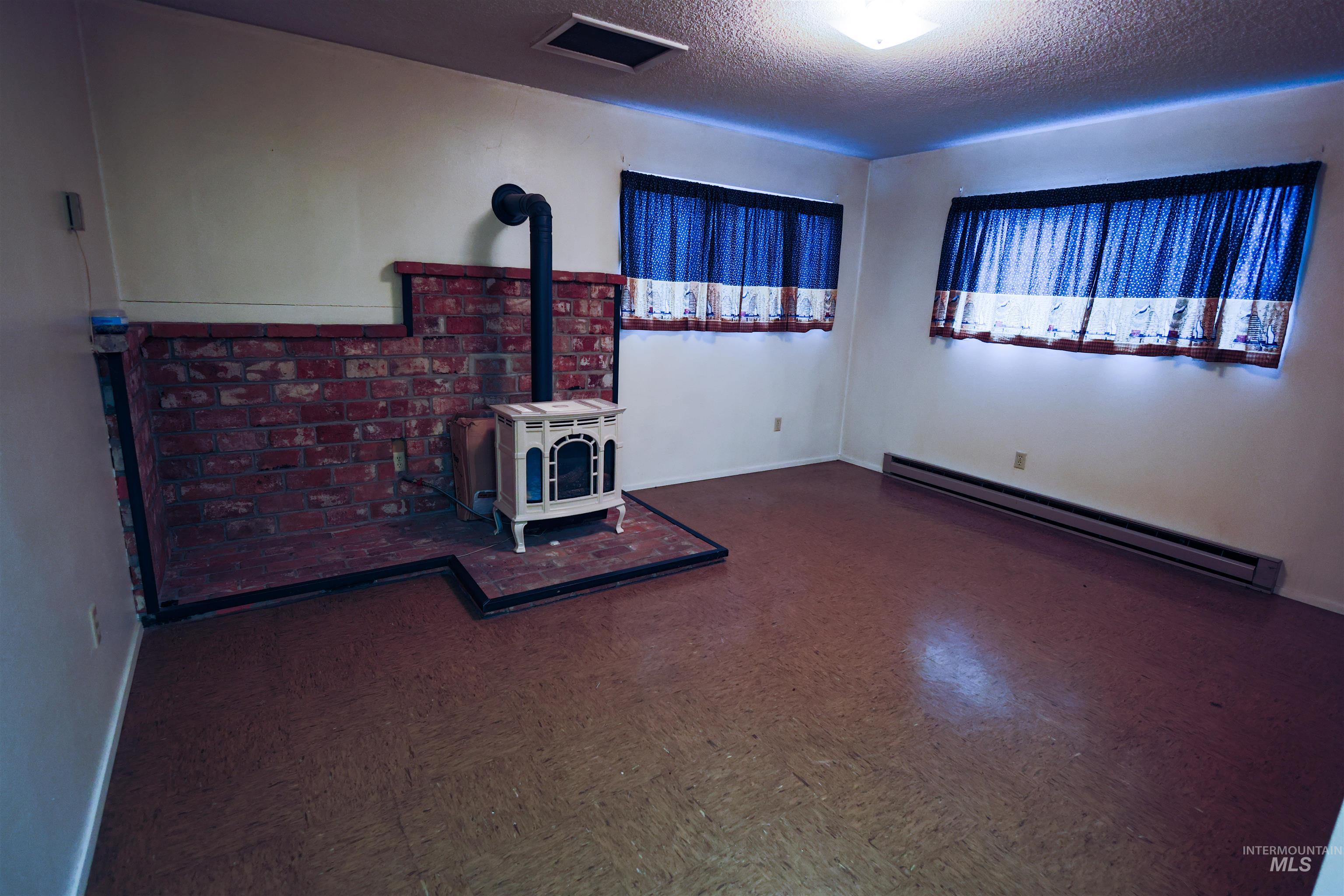 717 Big Cedar Road Kooskia, ID 83539 - Photo 14 of 50 Unfurnished living room with baseboard heating, a textured ceiling, dark flooring, and a wood stove