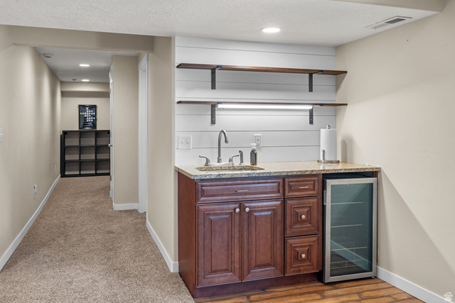 955 Delorean Lane Midvale, UT 84047 - Photo 38 of 47 Built-in wet bar featuring a granite countertop, undermount sink with a gooseneck faucet, dark wood cabinetry, and an integrated beverage refrigerator