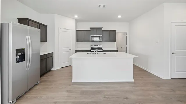 a view of a kitchen with stainless steel appliances granite countertop a stove top oven a refrigerator a sink and dishwasher