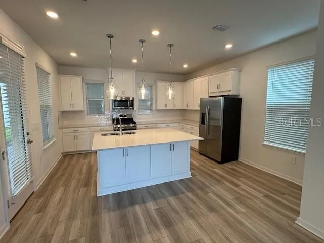 an empty room with wooden floor kitchen appliances and windows