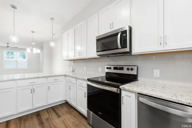 a kitchen with stainless steel appliances granite countertop a sink dishwasher a stove and a microwave oven with white cabinets