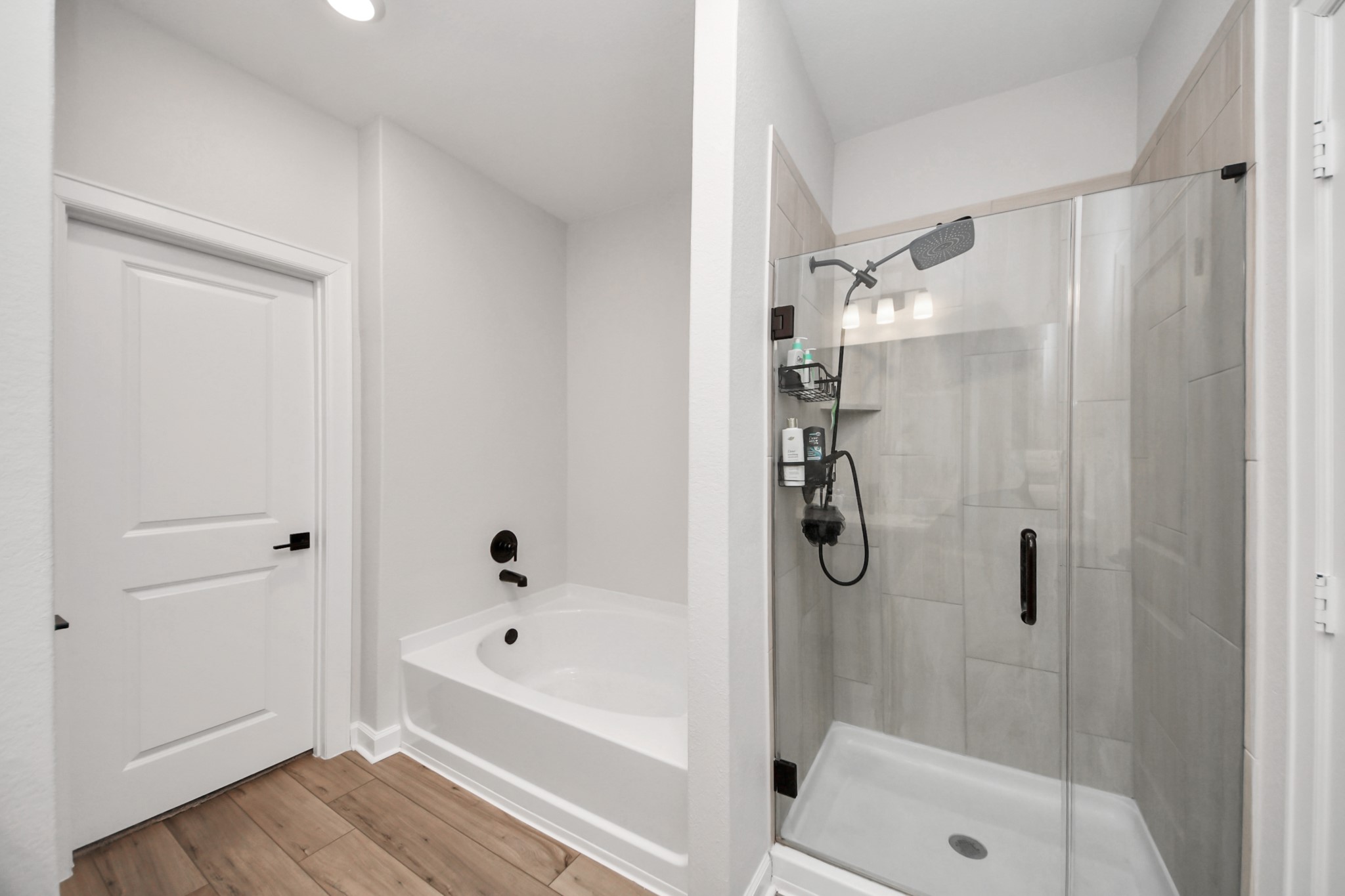 3006 Floating Barque Drive Santa Fe, TX 77510 - Photo 19 of 37 This modern bathroom features a sleek glass-enclosed shower with a rainfall showerhead, a spacious bathtub, and elegant wood-look tile flooring. The neutral palette adds a clean, inviting feel.