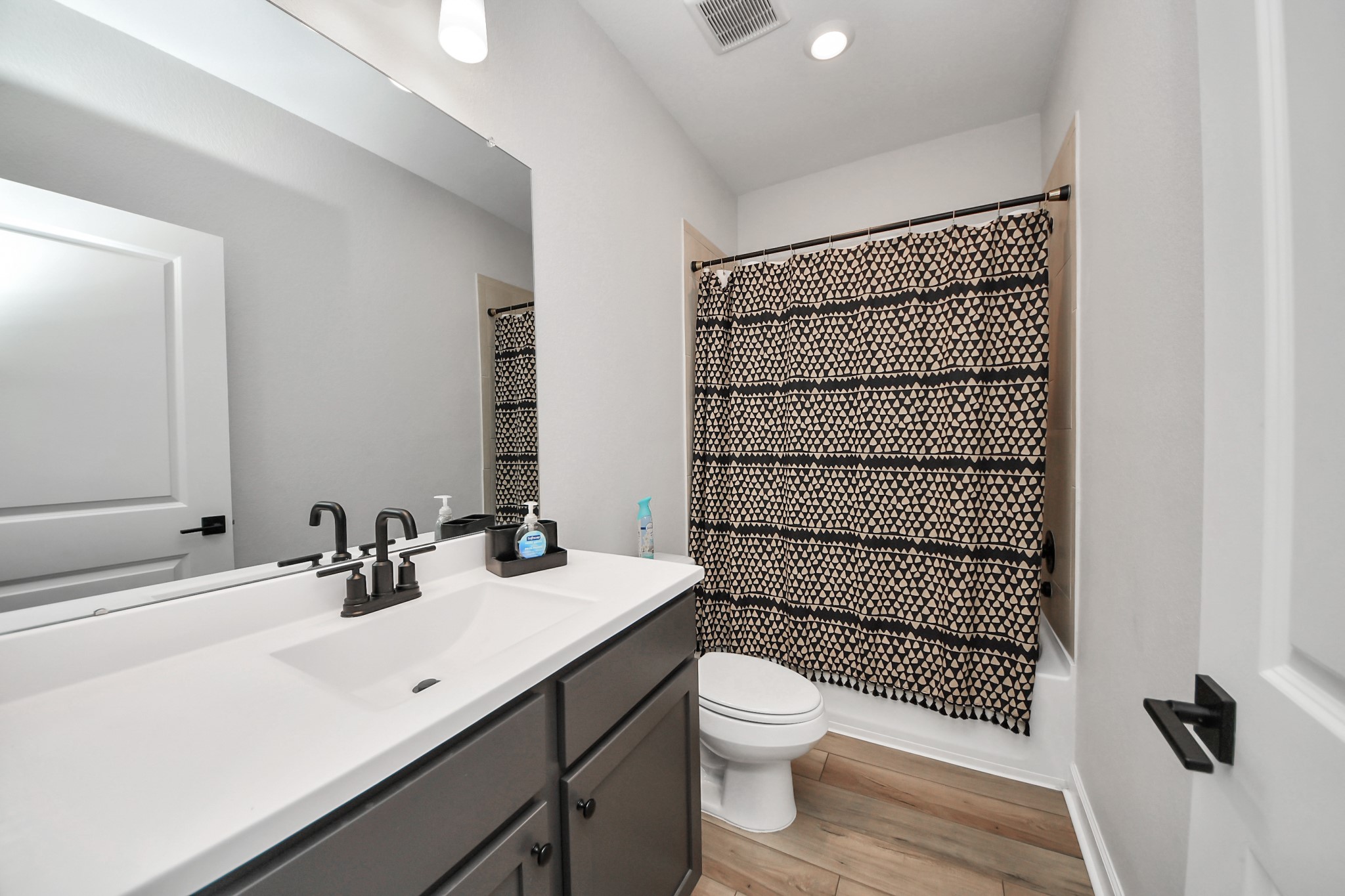 3006 Floating Barque Drive Santa Fe, TX 77510 - Photo 25 of 37 This bathroom features a modern design with a sleek white vanity, dark fixtures, and a large mirror. It includes a bathtub and wood-look flooring.