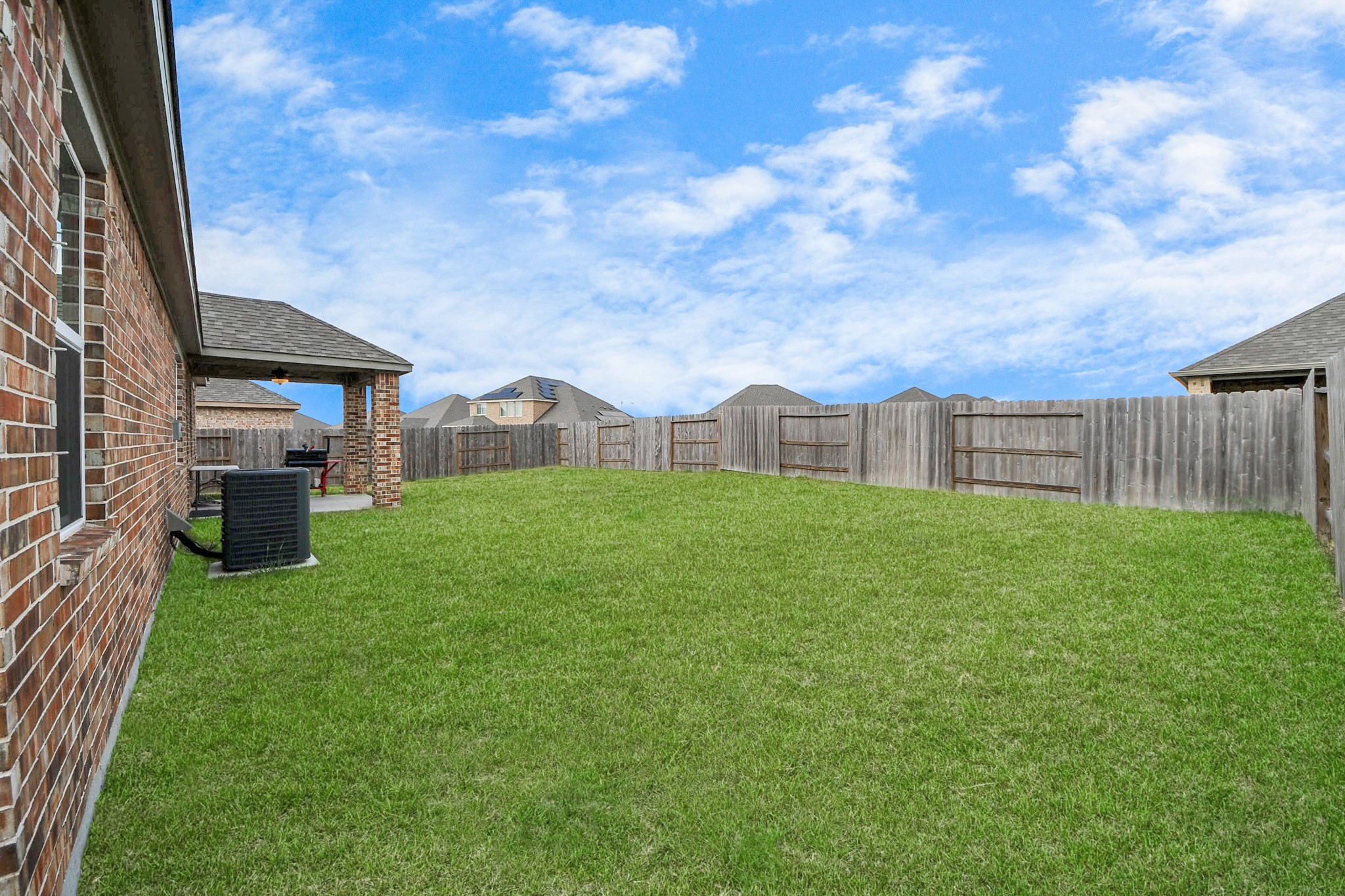 3006 Floating Barque Drive Santa Fe, TX 77510 - Photo 29 of 37 Spacious backyard with a well-maintained lawn, bordered by a wooden fence for privacy. The brick exterior of the house adds charm, and a covered patio area is perfect for outdoor relaxation.